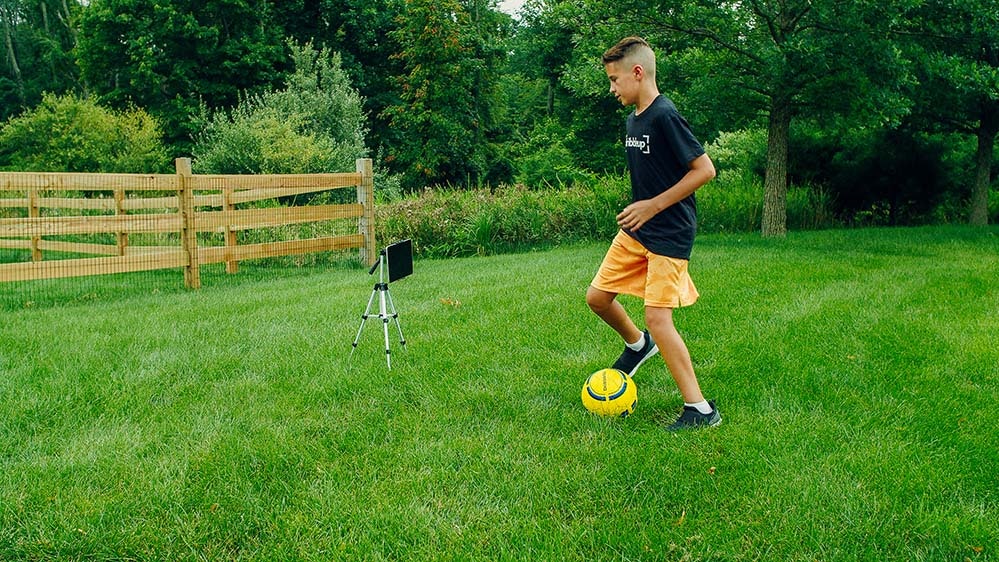 Young boy dribbling a soccer ball in his yard.
