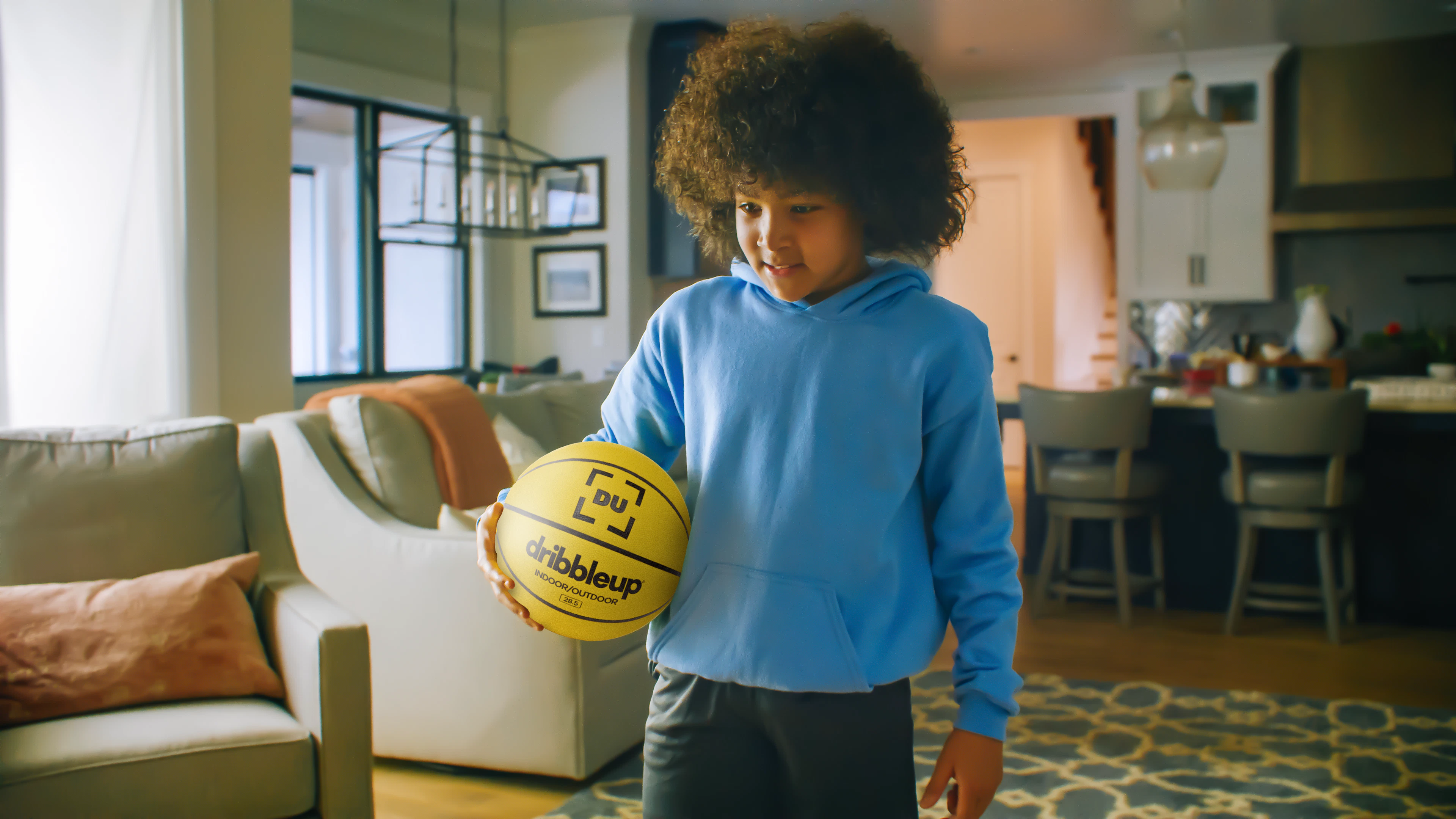 Young child holding a Dribbleup Smart Basketball in a living room