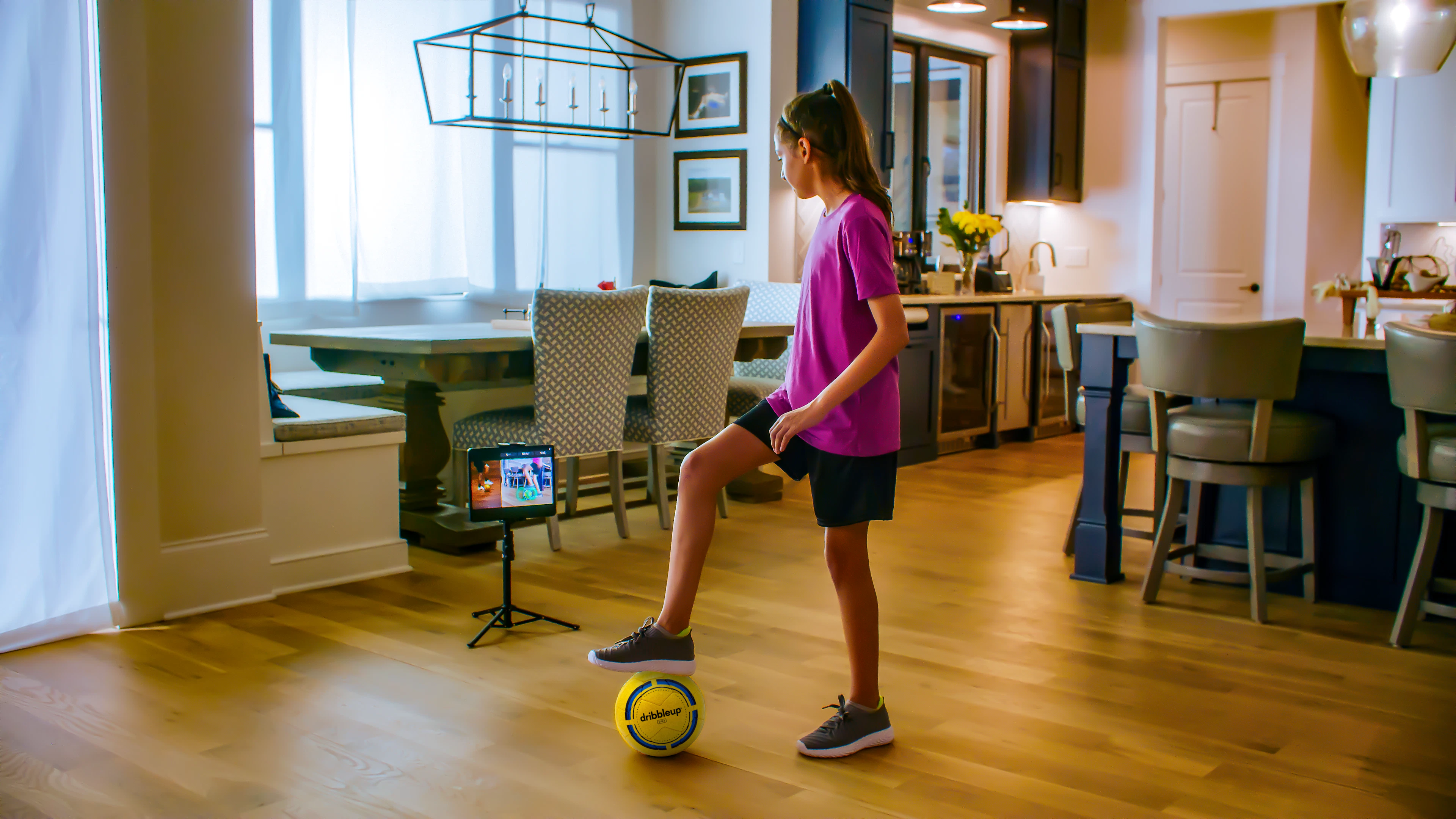 Girl training with a Dribbleup Smart Soccer Ball in her living room, trainer on the tablet
