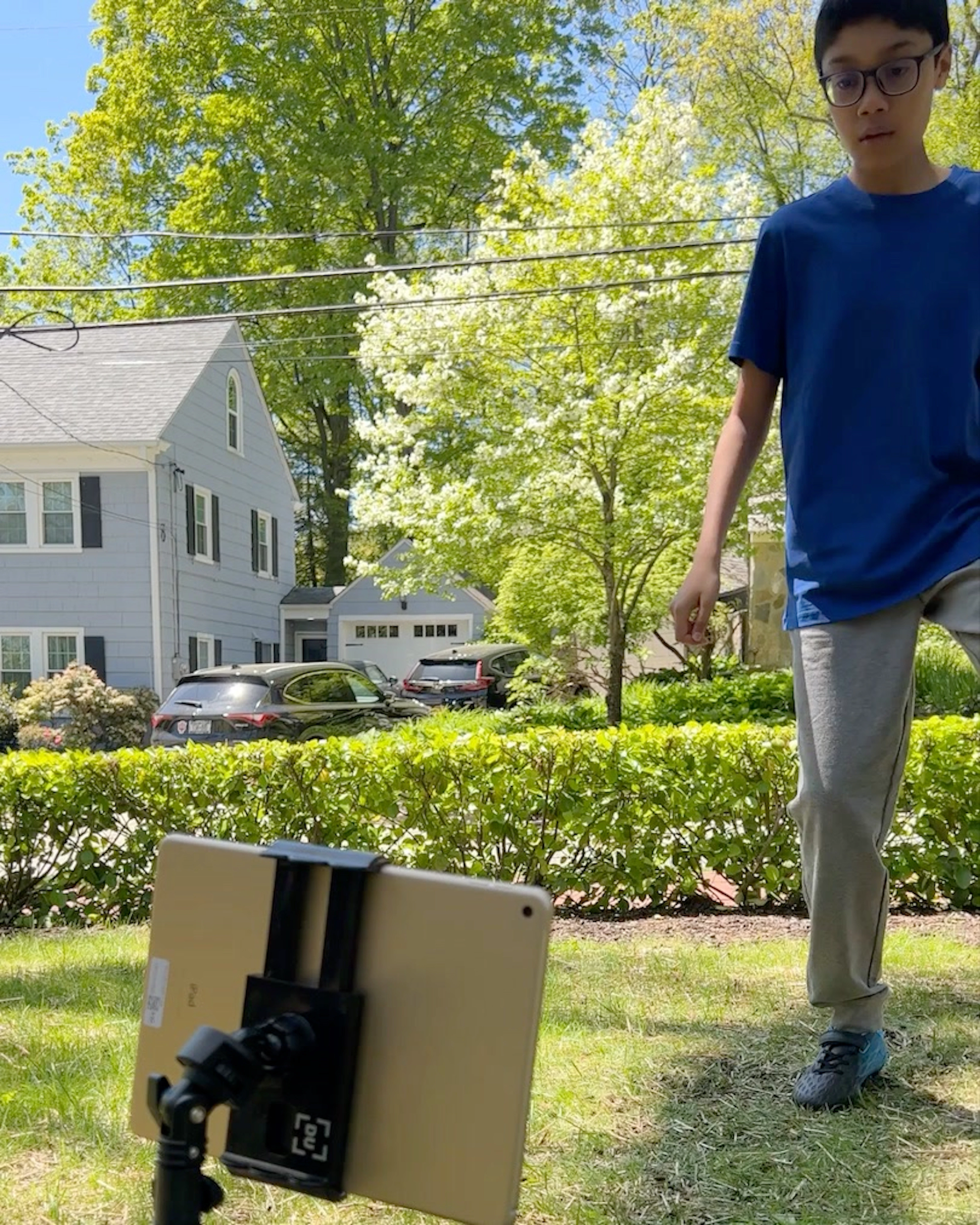 Boy standing on a lawn next to a tablet on a stand outdoors in a residential neighborhood
