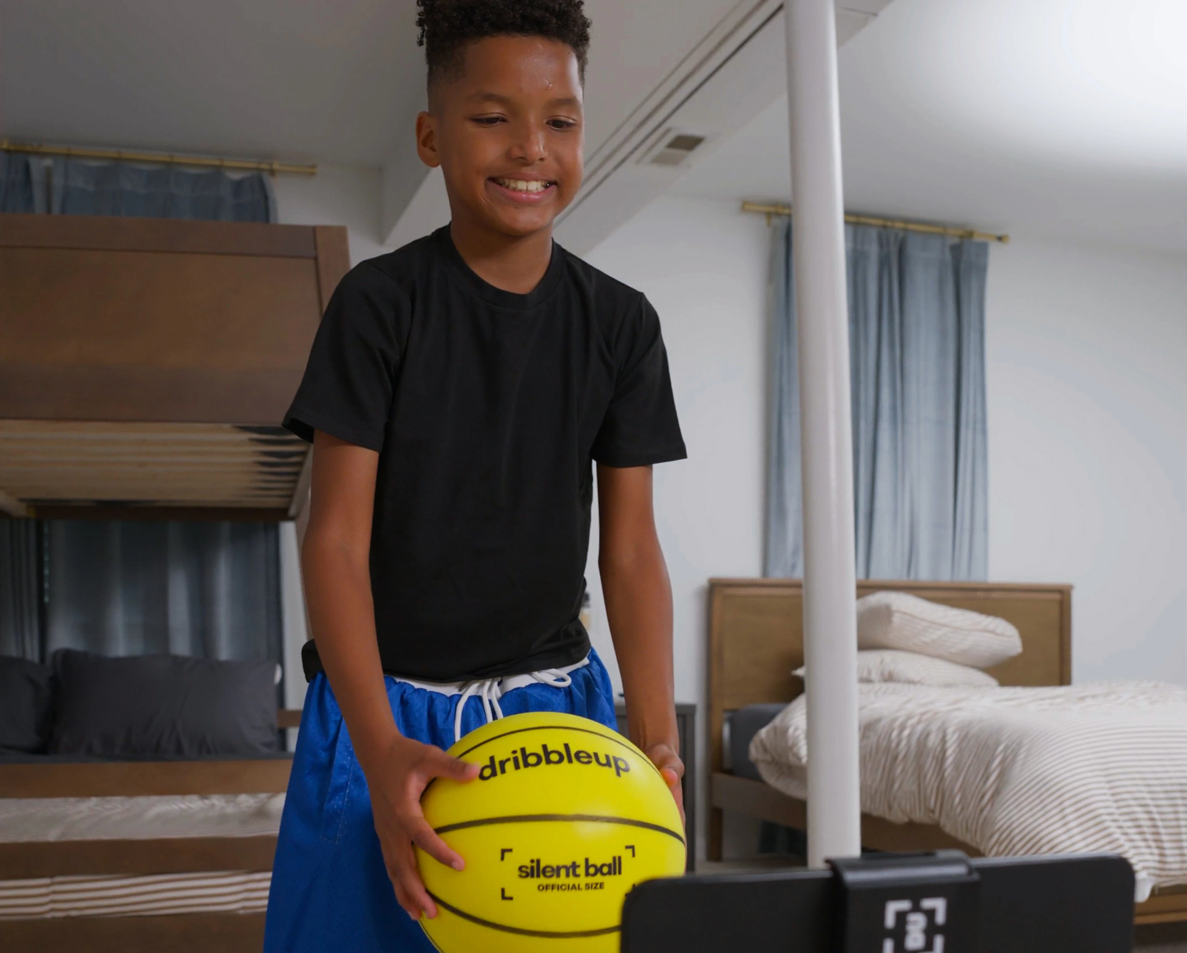 Smiling boy holding the Silent Smart Basketball while scanning in on a tablet in his bedroom